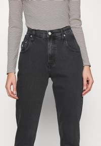 Černé džíny s vysokým pasem, hladkou texturou, předními kapsami, zipem a jemnými prošívacími detaily.