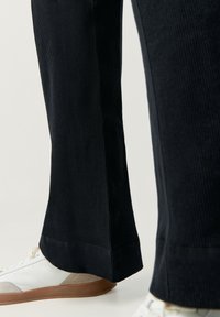 Svarta velourbyxor med ribbad textur, med rak passform och uppvikt fåll, i kombination med vita och beige sneakers.