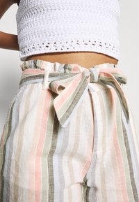 Lněné široké kalhoty s vysokým pasem, zdobené pastelovými pruhy v růžové, zelené a modré barvě. Mašle zavázaná v pase, neformální textura.