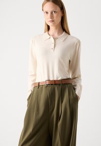 Kremowa koszulka polo z długim rękawem i kołnierzykiem, z trzema guzikami, w połączeniu z oliwkowymi spodniami z wysokim stanem oraz brązowym skórzanym paskiem.