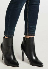 Zwarte leren enkellaarsjes met puntige neuzen en hoge hakken, gedragen met donkerblauwe skinny jeans.