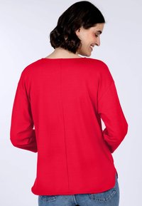 Rotes Langarmshirt mit weitem Ausschnitt, lässiger Passform und seitlichen Schlitzen, das eine glatte Textur und ein schlichtes Design aufweist.
