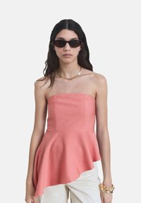 Top peplum corallo senza spalline con una finitura leggermente strutturata, caratterizzato da un orlo asimmetrico e un corpetto strutturato.