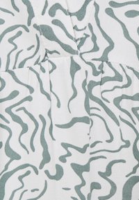 Gros plan sur un tissu blanc avec des rayures vertes ondulées irrégulières semblables à des zèbres et des coutures visibles.