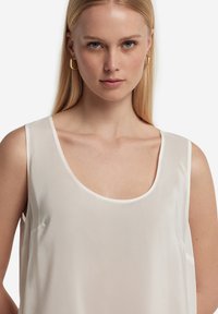 Lätta, ärmlös vit topp med rundad halsringning, mjuk satintextur och sidofickor för rörelsefrihet. Minimalistisk design.