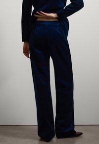 Marineblaue Samthose mit hoher Taille und lockerer Passform, dezenter Schimmer und Gesäßtaschen. Glatte Textur mit weitem Bein und klaren Linien.