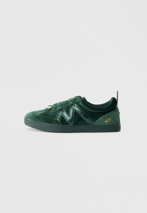 Green velvet sneaker with a textured rubber sole. Features a shiny green logo and gold hardware accents. Low-top design with laced closure.