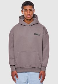 Šedá oversized mikina s kapucí, přední kapsou, žebrovanými manžetami a lemem, se textem "DROPSIZE" v černé na levé části hrudi.