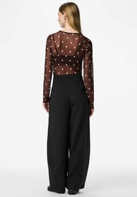 Donna vista da dietro che indossa una camicia trasparente nera a maniche lunghe con pois bianchi e pantaloni neri a vita alta e larghi.