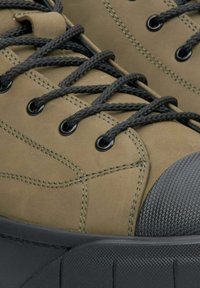 Olivově zelené tenisky s texturovaným gumovým špičkou, silnou černou podrážkou a tmavými tkaničkami. Mají prošité detaily po stranách.