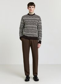 Knitted sweater in black and cream geometric pattern, paired with brown trousers and black shoes. Smooth texture with ribbed cuffs and hem.