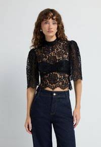 Sort blonderet crop top med korte puffede ærmer, blomstermønster og høj hals, parret med højtaljede mørke denim jeans.