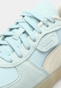 Adidași de culoare albastră deschisă, realizati din suede și piele netedă, cu accente texturate și o talpă din cauciuc cu detalii embossate ale logo-ului.