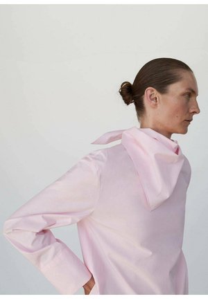 Chemise à manches longues de couleur rose pâle en tissu lisse, avec un col et une écharpe assortie nouée au cou, présentant des poignets structurés.