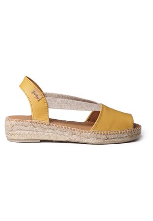 Keltainen nahkainen slingback-sandaali, jossa on kudottu elastinen hihna, juuttipäällysteinen pohja ja avonainen varvasmuotoilu. Sujuva tekstuuri ja rento tyyli.