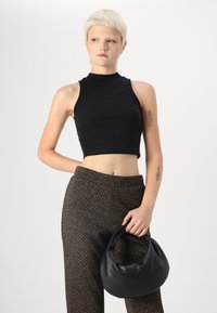 Čierny bezrukávový crop top s vysokým golierom, skombinovaný s textúrovanými hnedými vzorovanými nohavicami a čiernou koženou taškou s okrúhlou rúčkou.