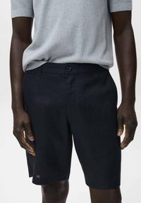 Pantaloni corti blu scuro realizzati in un tessuto leggero, con un davanti piatto, tasche laterali e chiusura con un singolo bottone.
