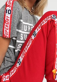 Grijze katoenen T-shirt met een wit en rood grafisch ontwerp. Rode trainingsbroek met een witte en blauwe logo-streep aan de zijkanten.