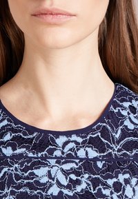 Blouse navy avec broderie en dentelle florale bleu clair, col rond et finition texturée avec des détailsintriqués.