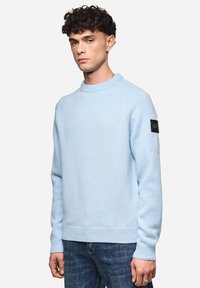 Himmelblauer Strickpullover mit Rundhalsausschnitt, gerippten Bündchen und Saum. Verfügt über ein schwarzes Logo-Patch auf dem linken Ärmel. Eignet sich gut für die Freizeit.