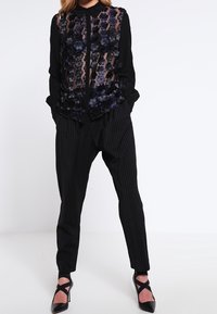 Svart skjorta i genomskinligt tyg med blommig broderi, i kombination med svarta ränderade byxor och svarta sandaler med remmar.