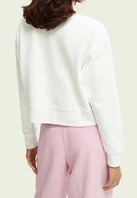 Sudadera blanca corta con una textura suave, mangas amplias y escote redondeado. Combinada con pantalones rosa claro.