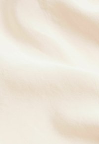 Tissu couleur crème avec une texture lisse et légèrement brillante ; surface doucement ondulée indiquant la douceur et un tombé fluide.