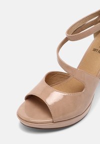 Sandale en cuir verni beige avec un bout rond, un avant ouvert et deux brides croisées. Texture lisse et semelle rembourrée pour le confort.