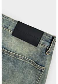 Lichtblauwe spijkerbroek van denim met een gestructureerd oppervlak, voorzien van een effen zwart leren label met reliëfbranding op de tailleband.