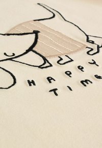 Weißer Stoff mit einem verspielten gestickten Design eines Hundes mit einem beigen Streifen, neben dem Text "HAPPY TIME" in schwarzem Faden.