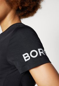 Camisa preta de mangas curtas com textura suave e um estampado gráfico de "BORO" em letras brancas pontilhadas na manga direita.