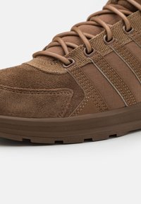 Hnědé semišové a textilní tenisky s tkaničkovým zapínáním, zesílenou špičkou a texturovanou gumovou podrážkou. Obsahují kontrastní panely a švy.