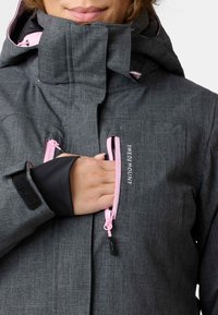 Graue wasserdichte Jacke mit pinkfarbenen Reißverschlüssen und Branding. Verfügt über einen hohen Kragen, verstellbare Manschetten und eine weiche, strukturierte Oberfläche.