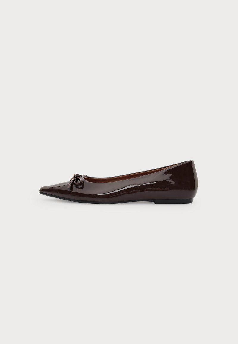 Chaussure plate marron brillante à bout pointu avec un petit nœud sur le devant et un petit talon sur un fond uni.