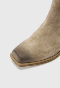 Stivale alla caviglia in suede beige con punta quadrata, texture liscia e graduale scurimento alla punta, dotato di una suola marrone minimalista.