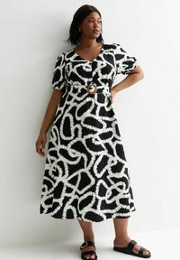 Robe à motif noir et blanc avec de courtes manches bouffantes, un décolleté en V, et une taille cintrée mettant en valeur une ceinture circulaire marron.