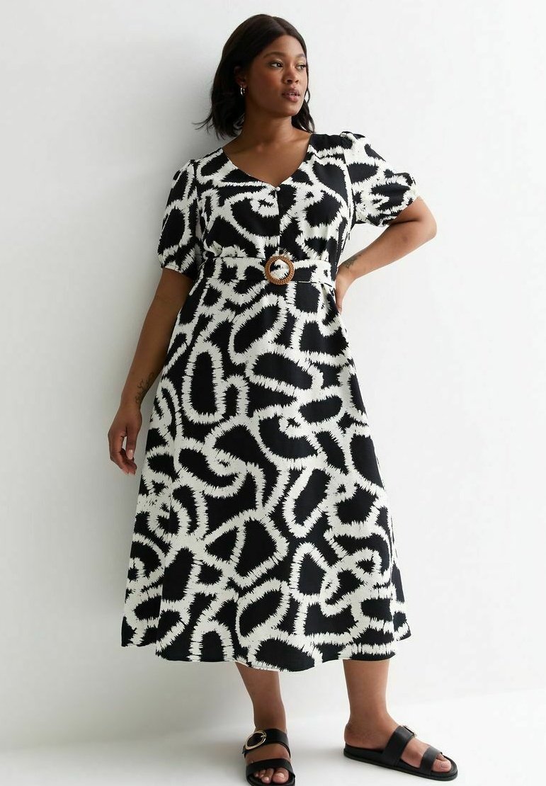 Robe à motif noir et blanc avec de courtes manches bouffantes, un décolleté en V, et une taille cintrée mettant en valeur une ceinture circulaire marron.