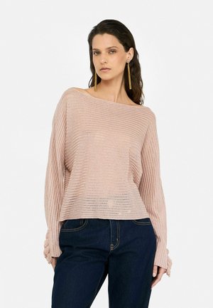 Maglione a coste rosa chiaro con design off-shoulder, tessuto testurizzato e maniche lunghe con fessure. Abbinato a jeans blu scuro.