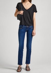 Black V-neck t-shirt with short sleeves, blue slim-fit jeans, and black strappy sandals, held with a gray handbag. Smooth fabric texture.