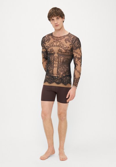 Top a maniche lunghe in chiffon con un design in pizzo nero su base beige, abbinato a pantaloni corti aderenti marroni. Presenta intricati motivi in pizzo.