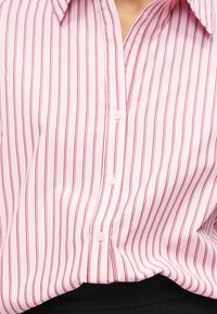 Εικόνα κοντινού πλάνου ενός ατόμου που φοράει ροζ πουκάμισο με κάθετες κόκκινες ρίγες, περασμένο μέσα σε μαύρο παντελόνι.