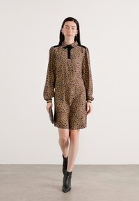 Leopardenmuster-Kleid mit Kragen, langen Ballonärmeln und schwarzen Akzenten, kombiniert mit schwarzen Knöchelstiefeln und einer Clutch.