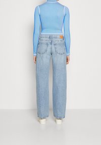 Jasnoniebieski prążkowany top z długim rękawem w połączeniu z wysokim stanem, prostymi, jasnoniebieskimi dżinsami z klasycznym pięciopocketowym wzorem.