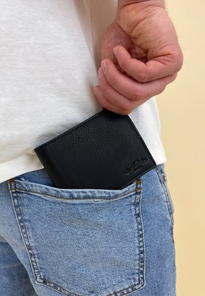 Black leather wallet with a textured surface partially displayed in a light blue denim pocket. Simple rectangular design with subtle branding.