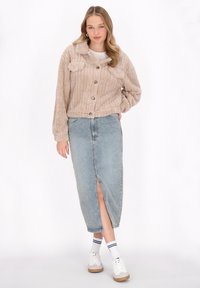Giacca cropped beige con texture, maniche lunghe e bottoni frontali, abbinata a una gonna lunga in denim con spacco frontale. Sneakers bianche e calze a righe.
