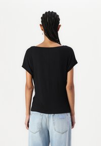 Top nero a maniche corte con scollatura ampia e una texture liscia, abbinato a jeans high-waisted blu chiaro con tasche posteriori.
