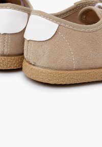 Scarpe in suede beige con suola in gomma testurizzata e dettaglio in pelle bianca sul tallone, progettate per offrire comfort e facilità d'uso.