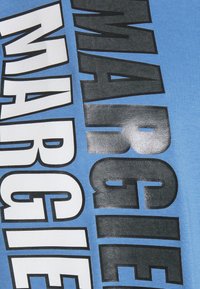 Blå bomulls-T-shirt med fet, stor svart och vit text. Tyget har en mjuk textur och en avslappnad design.