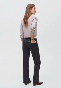Maglione grigio corto su una maglietta bianca, abbinato a jeans svasati scuri con tasche posteriori e sottili decorazioni, indossato con ballerine marroni.