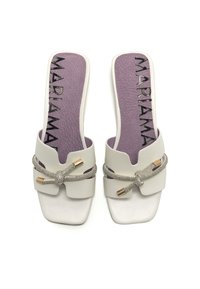 Sandalias blancas de punta abierta con forma cuadrada, que cuentan con una plantilla texturizada en color lila y un nudo metálico decorativo con acentos.